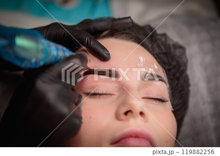 Cosmetologist applying permanent makeup on eyebrows  using tattoo machine 119882256