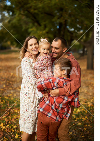 Happy family walking on green grass strewn with fallen leaves in Park in autumn. Parents, two Happy family walking on green grass strewn with fallen leaves in Park in autumn. Parents, two 119882831
