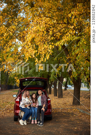 Happy parents with daughter and cute dog Jack Russel terrier sitting in car trunk on autumn day Happy parents with daughter and cute dog Jack Russel terrier sitting in car trunk on autumn day 119882842