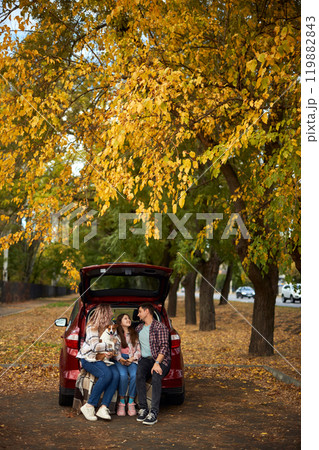Happy parents with daughter and cute dog Jack Russel terrier sitting in car trunk on autumn day Happy parents with daughter and cute dog Jack Russel terrier sitting in car trunk on autumn day 119882843