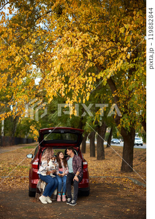 Happy parents with daughter and cute dog Jack Russel terrier sitting in car trunk on autumn day Happy parents with daughter and cute dog Jack Russel terrier sitting in car trunk on autumn day 119882844