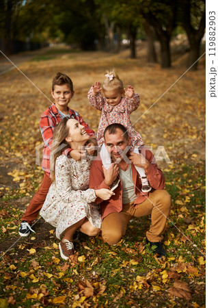 Happy family walking on green grass strewn with fallen leaves in Park in autumn. Parents, two 119882903