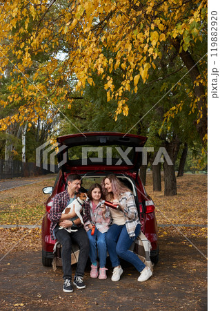 Happy parents with daughter and cute dog Jack Russel terrier sitting in car trunk on autumn day Happy parents with daughter and cute dog Jack Russel terrier sitting in car trunk on autumn day 119882920