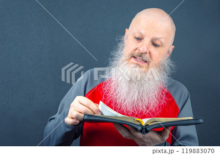 venerable christian man with a large gray beard focused on reading the bible 119883070