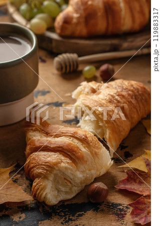 Cozy autumn breakfast with croissant, coffee and autumn fruits, grapes, pears and hazelnuts on wooden table 119883317