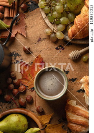 Cozy autumn breakfast composition with coffee, croissants, autumn fruits, grapes, pears and hazelnuts on wooden table. Top view Cozy autumn breakfast composition with coffee, croissants, autumn fruits, grapes, pears and hazelnuts on wooden table. Top view 119883318