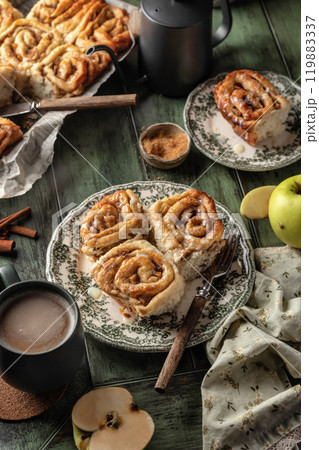 Autumn apple cinnamon rolls with frosting on green wooden background. Seasonal autumn homemade pastry cinnabons for breakfast Autumn apple cinnamon rolls with frosting on green wooden background. Seasonal autumn homemade pastry cinnabons for breakfast 119883337