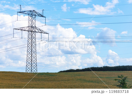 Electricity concept. High voltage power line pylons, electrical tower on a green field with blue sky. 119883718