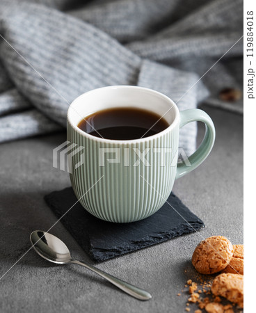 Espresso coffee in a mug on a dark background with cookies, spoon and a cozy gray sweater. 119884018