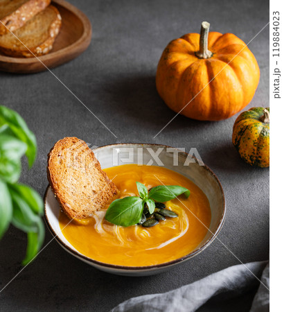 Homemade pumpkin soup with cream, basil and seeds on a dark background with bread, napkin  119884023