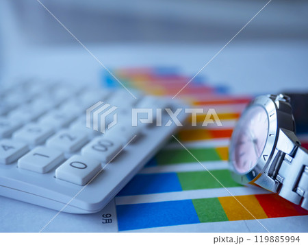 テーブルに置かれたグラフと電卓と腕時計 テーブルに置かれたグラフと電卓と腕時計 119885994