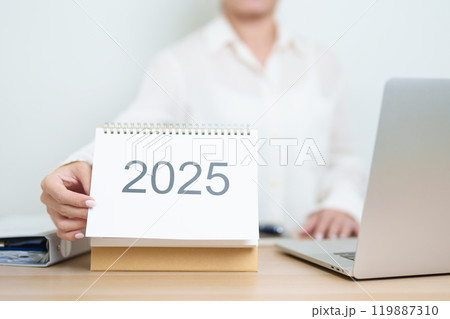 2025 Year Calendar on table with business woman using laptop computer, working and writing in office. countdown, Happy New Year, Resolution, Year End and New Start and Goals Plan Action Concept 119887310