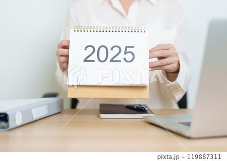 2025 Year Calendar on table with business woman using laptop computer, working and writing in office. countdown, Happy New Year, Resolution, Year End and New Start and Goals Plan Action Concept 119887311