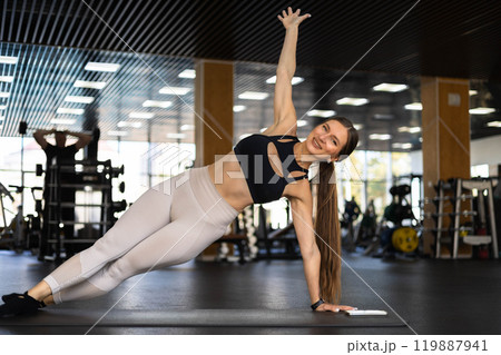 Smiling fitness woman stand in plank position doing push ups training at gym 119887941