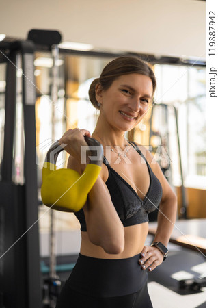 Portrait of muscular female athlete smiling posing with kettlebell training at modern gym closeup 119887942