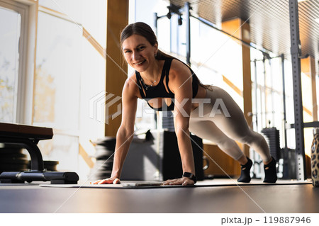 Smiling fitness woman stand in plank position doing push ups training at gym Smiling fitness woman stand in plank position doing push ups training at gym 119887946