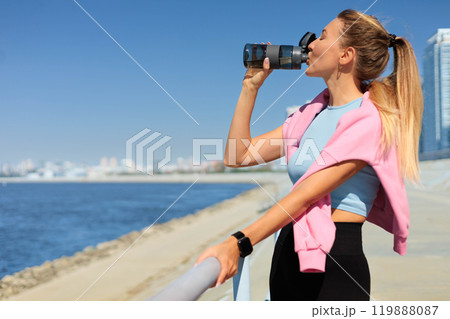 Sport woman jogger runner drinking water from bottle at city embankment river closeup 119888087