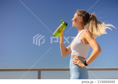 Smiling young blonde woman jogger runner drink water from bottle at river embankment closeup Smiling young blonde woman jogger runner drink water from bottle at river embankment closeup 119888088