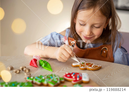 A little girl decorates a Christmas gingerbread mitten. Concept of preparations for Christmas A little girl decorates a Christmas gingerbread mitten. Concept of preparations for Christmas 119888214