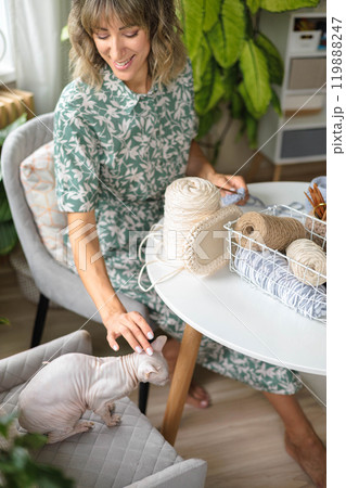 Young beautiful girl in a dress sits at a round white table and crochets. Sphinx cat.  119888247