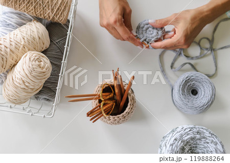 Women's hands crochet with gray yarn on a white background. Skeins of cotton yarn in natural 119888264