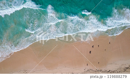 Aerial view of a sandy beach with turquoise waves crashing onto the shore scattered people are seen walking along the coastline 119888279