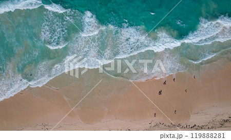 Aerial view of a sandy beach with turquoise waves crashing onto the shore scattered people are seen walking along the coastline 119888281