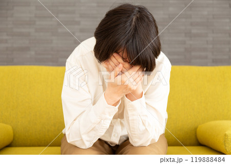 家のソファーで顔を覆って悲しむミドル〜シニア女性 119888484