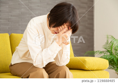 家のソファーで顔を覆って悲しむミドル〜シニア女性 119888485