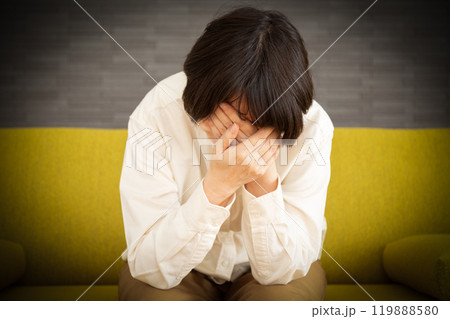 家のソファーで顔を覆って悲しむミドル〜シニア女性 家のソファーで顔を覆って悲しむミドル〜シニア女性 119888580