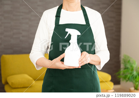 家のリビングで洗剤を持つ緑のエプロンをしたシニア女性の主婦・家政婦 119889020