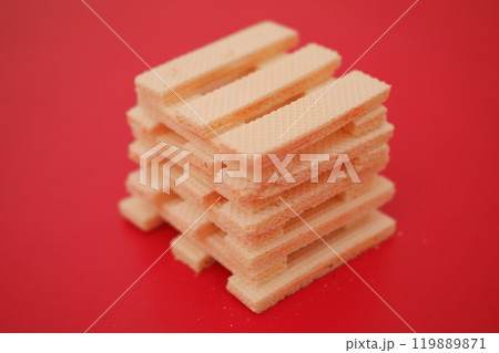 beige wafer cookies with a cream filling is scattered on a bright red surface 119889871
