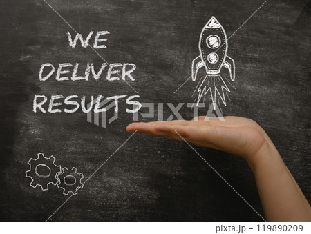 A hand holding a chalkboard with the words We deliver results written on it A hand holding a chalkboard with the words We deliver results written on it 119890209