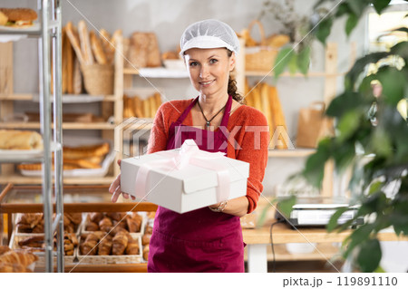 Female baker or confectioner with gift box of cake in bakery Female baker or confectioner with gift box of cake in bakery 119891110