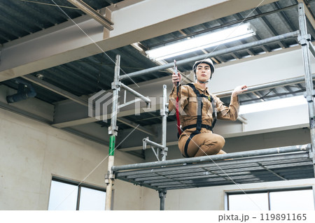 建設現場の足場に登って高所作業する作業員 建設現場の足場に登って高所作業する作業員 119891165