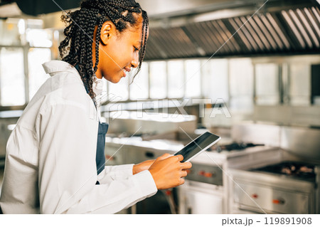 Female chef in world famous restaurant's modern kitchen cooks using tablet. Gourmet organic dishes prepared technology assists. Professional smiling reading communicating. Female chef in world famous restaurant's modern kitchen cooks using tablet. Gourmet organic dishes prepared technology assists. Professional smiling reading communicating. 119891908
