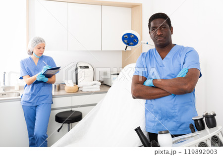 Confident cosmetologist in aesthetic medicine office with female assistant 119892003