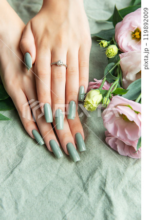 Elegant hands with green nail polish resting on a soft fabric surrounded by delicate flowers Elegant hands with green nail polish resting on a soft fabric surrounded by delicate flowers 119892009
