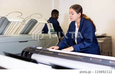Concentrated young female typographer in a blue robe uniform pressing the buttons on the plotter in the typography Concentrated young female typographer in a blue robe uniform pressing the buttons on the plotter in the typography 119892112