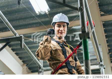 建設現場の足場に登ってガッツポーズする作業員 119892331