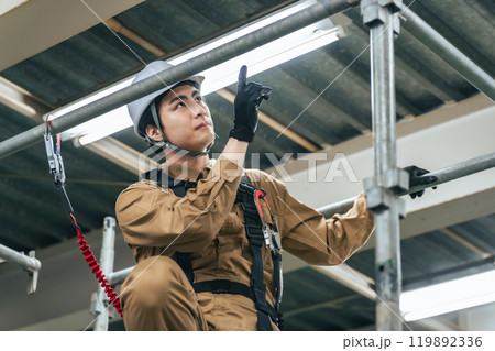 建設現場の足場に登って建物を点検する作業員 119892336