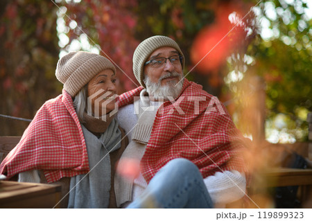 Elderly married couple sitting on a coffee shop terrace on beautiful autumn day, enjoying cup of coffee in the autumn atmosphere. 119899323