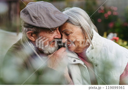 Portrait of beautiful senior couple outdoors in an autumn garden. Elderly husband and wife are embracing each other. Portrait of beautiful senior couple outdoors in an autumn garden. Elderly husband and wife are embracing each other. 119899361