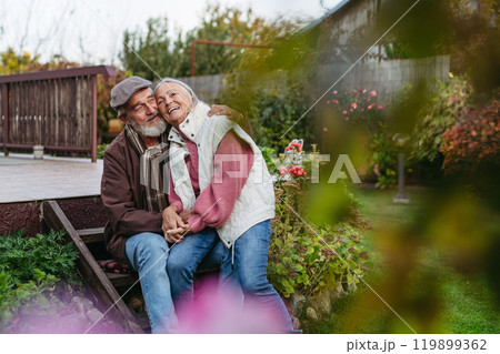 Portrait of beautiful senior couple outdoors in an autumn garden. Elderly husband and wife are embracing each other. Portrait of beautiful senior couple outdoors in an autumn garden. Elderly husband and wife are embracing each other. 119899362