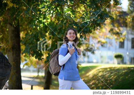 Beautiful nurse walking to work with backpack on her back. Autumn walk from hospital to home for young healthcare worker. Beautiful nurse walking to work with backpack on her back. Autumn walk from hospital to home for young healthcare worker. 119899431