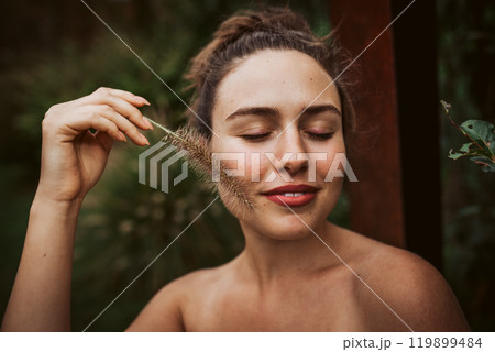 Portrait of a beautiful woman standing in a garden, holding a ornamental grass in her hand. Mental well-being and connection with nature. 119899484