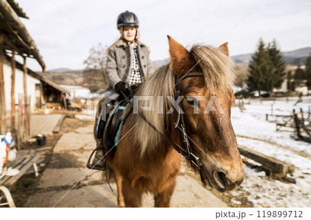Young girl spending cold winter weekend on family farm, riding her brown fluffy pony. Young girl spending cold winter weekend on family farm, riding her brown fluffy pony. 119899712