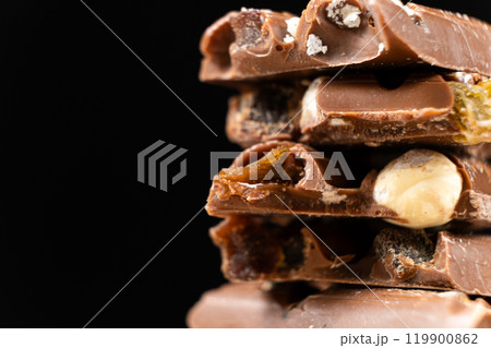Pieces of broken milk chocolate with nuts and raisins on a black background copy the space. Pieces of broken milk chocolate with nuts and raisins on a black background copy the space. 119900862