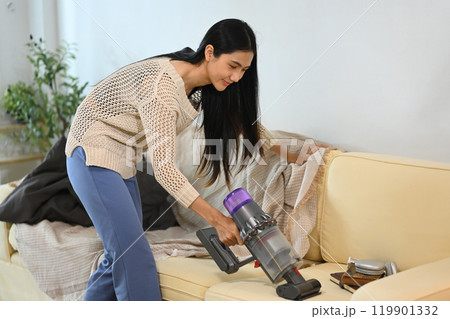 Young woman cleaning her living room sofa with a cordless vacuum Young woman cleaning her living room sofa with a cordless vacuum 119901332