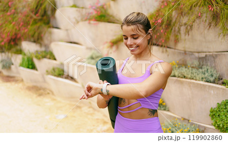 A joyful young woman is checking the time while practicing yoga outdoors on a beautiful day 119902860
